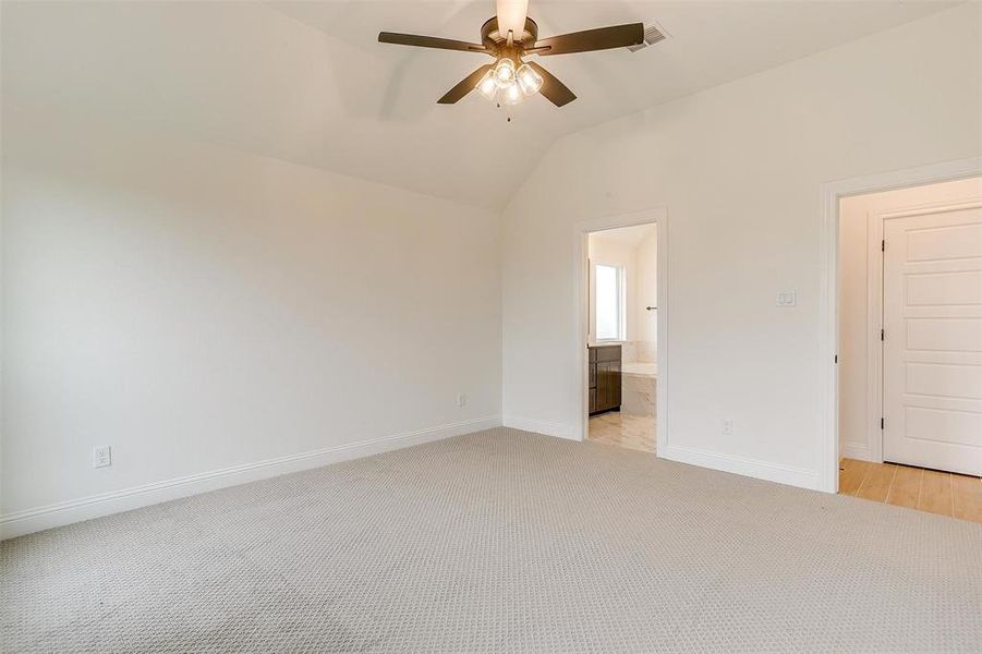 Unfurnished bedroom featuring ensuite bath, ceiling fan, vaulted ceiling, and light colored carpet