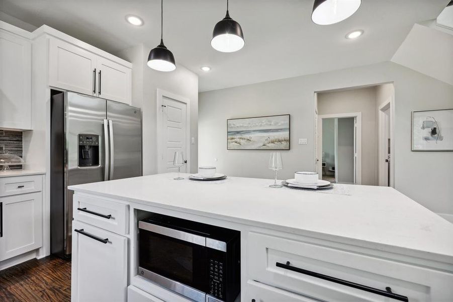 Kitchen featuring white cabinetry, dark hardwood / wood-style flooring, a kitchen island, stainless steel appliances, and decorative light fixtures