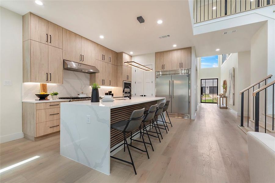 Kitchen with light hardwood / wood-style flooring, a high ceiling, stainless steel built in fridge, a kitchen bar, and a center island with sink
