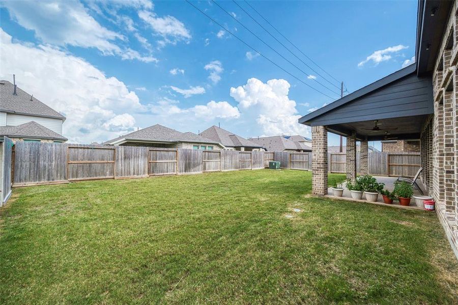 Spacious backyard with well-maintained lawn and privacy fencing, featuring a large covered patio area ideal for outdoor living and entertainment.