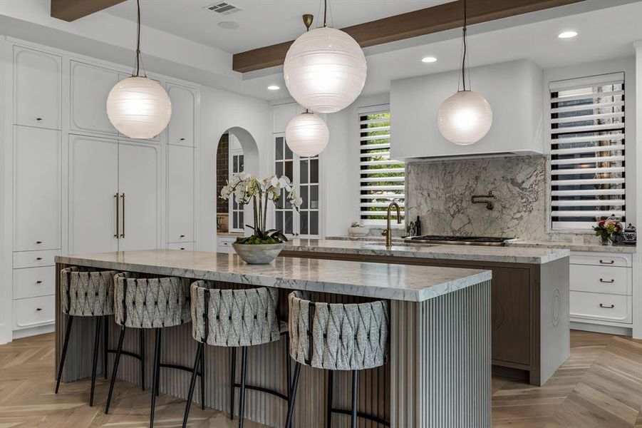 Kitchen with light parquet flooring, white cabinets, pendant lighting, and a large island