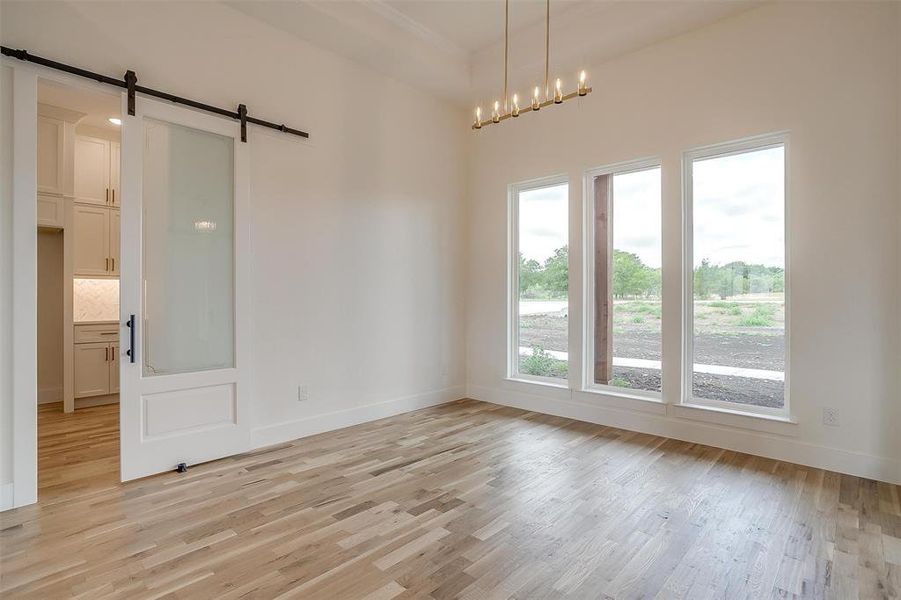 Unfurnished room with light hardwood / wood-style flooring, a barn door, and an inviting chandelier