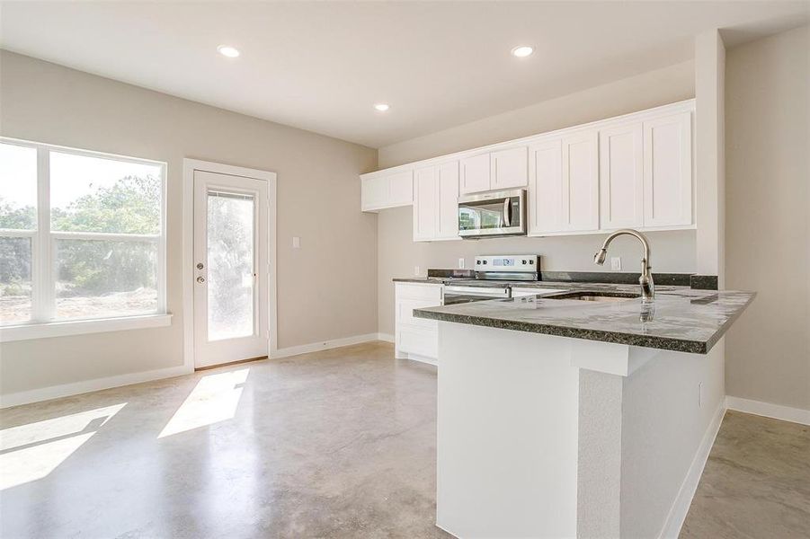 Kitchen with electric range, dark stone countertops, white cabinetry, sink, and kitchen peninsula