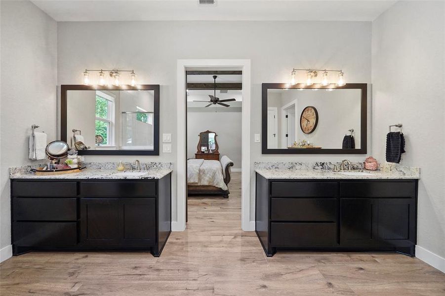 Twin vanities in the primary bathroom offer ample storage space for all the necessities. Each vanity features a granite countertop and a custom framed mirror with vanity lights above.