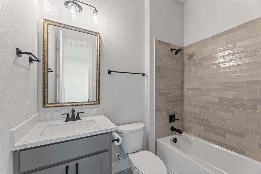 Full bathroom featuring tiled shower / bath combo, vanity, and toilet