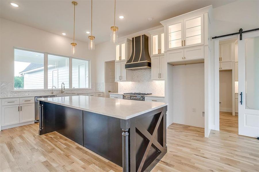 Kitchen with tasteful backsplash, white cabinets, light hardwood / wood-style floors, a barn door, and custom range hood