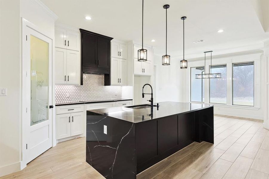 Kitchen featuring light wood-type flooring, sink, white cabinetry, backsplash, and a center island with sink