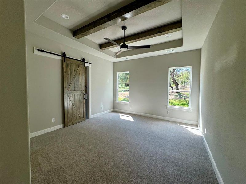 Unfurnished room with a barn door, a raised ceiling, carpet floors, beam ceiling, and ceiling fan