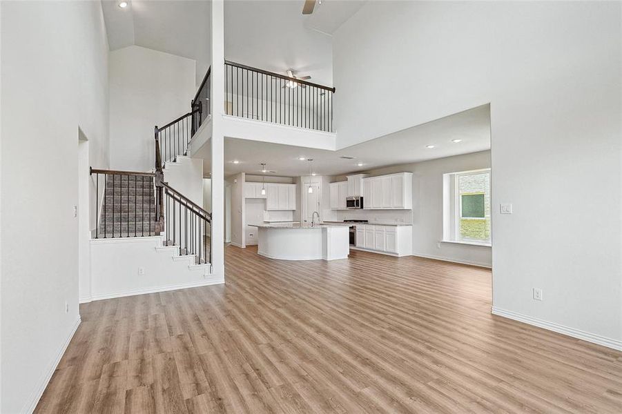 Unfurnished living room featuring high vaulted ceiling, light hardwood / wood-style floors, ceiling fan, and sink