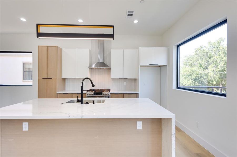 Kitchen featuring an island with sink, wall chimney exhaust hood, light stone countertops, and white cabinets