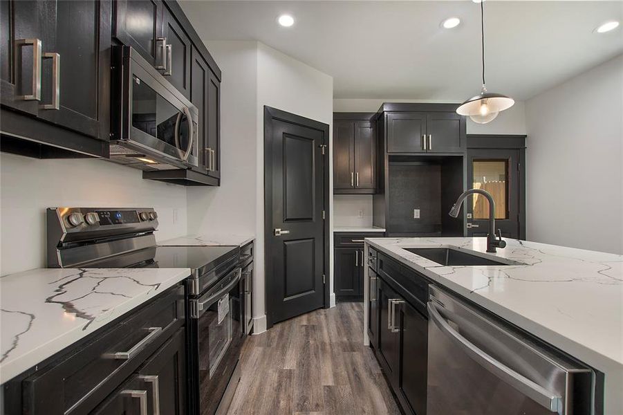 Kitchen with sink, hanging light fixtures, dark hardwood / wood-style flooring, light stone counters, and stainless steel appliances