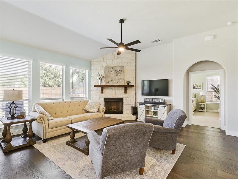 Living room with a wealth of natural light, vaulted ceiling, a stone fireplace, and dark hardwood / wood-style floors