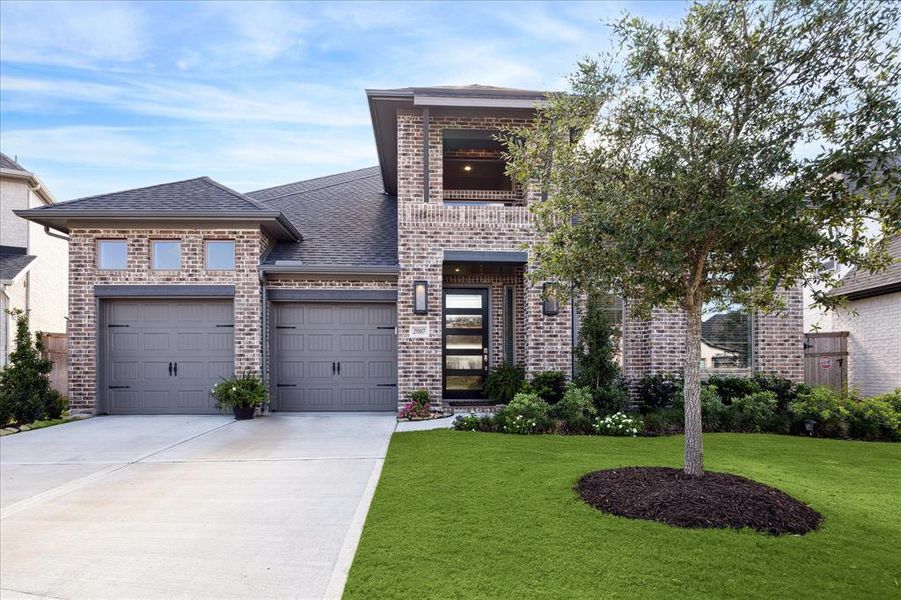 This is a two-story brick home featuring a well-manicured lawn, a mature tree in the front yard, and a 3 car tandem.