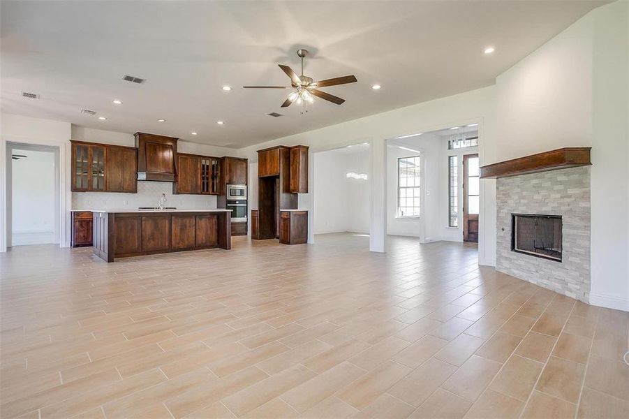 Unfurnished living room featuring light tile floors, sink, ceiling fan, and a fireplace
