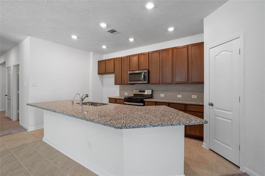 This spacious kitchen features high ceilings, stained wood cabinets, granite countertops, SS appliances, modern tile backsplash, recessed lighting, and pantry all overlooking your huge family room.