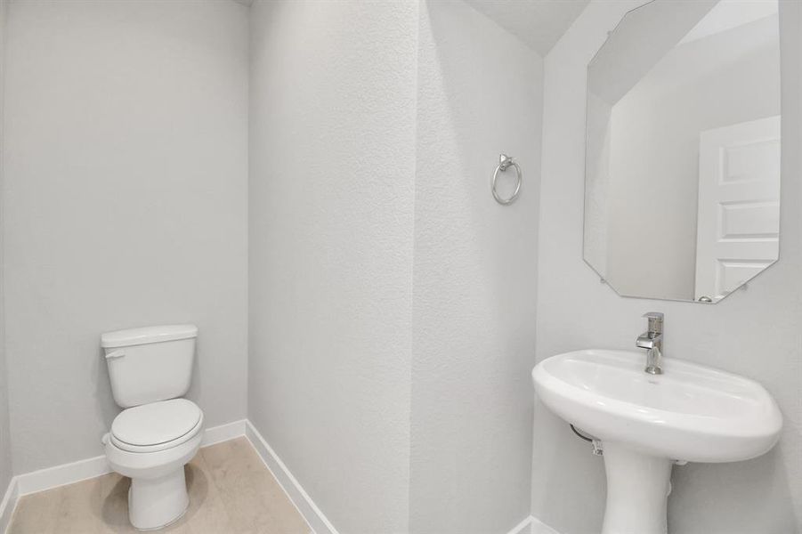 This half bathroom features a stylish pedestal sink, modern hardware, and bright recessed lighting, creating a sleek and inviting space.