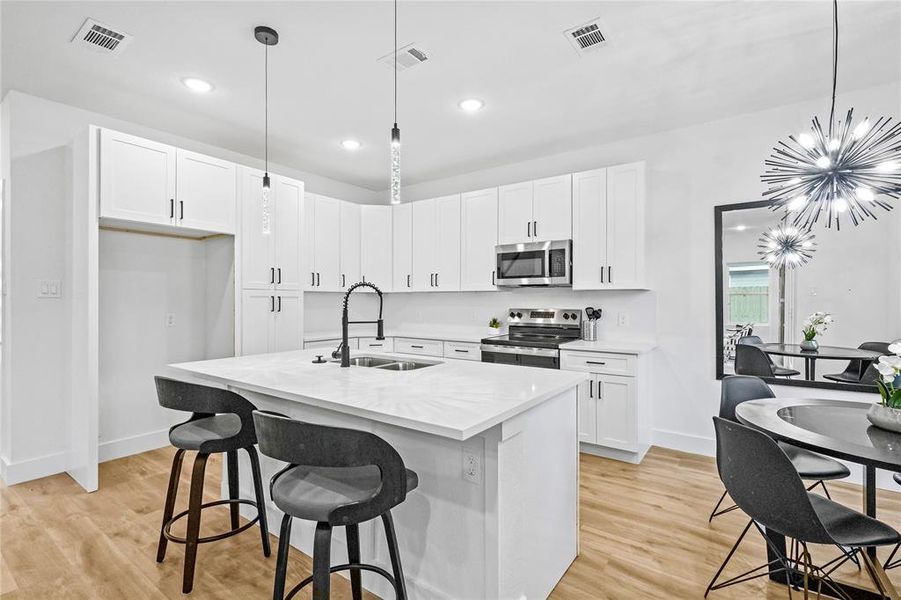 Kitchen featuring a kitchen island with sink, pendant lighting, stainless steel appliances, and a notable chandelier