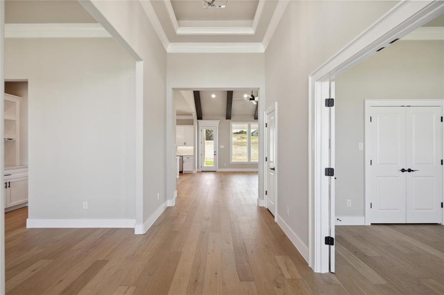 Corridor with a towering ceiling, light wood-type flooring, and crown molding