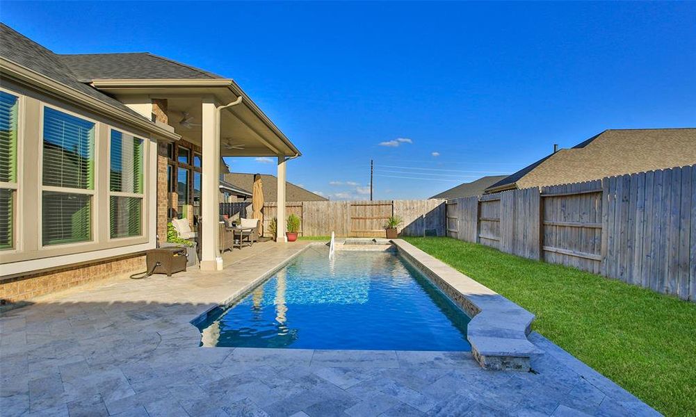 This is a backyard with a covered patio and a rectangular in-ground pool, complemented by a paved deck and a well-maintained lawn, enclosed by a wooden privacy fence.