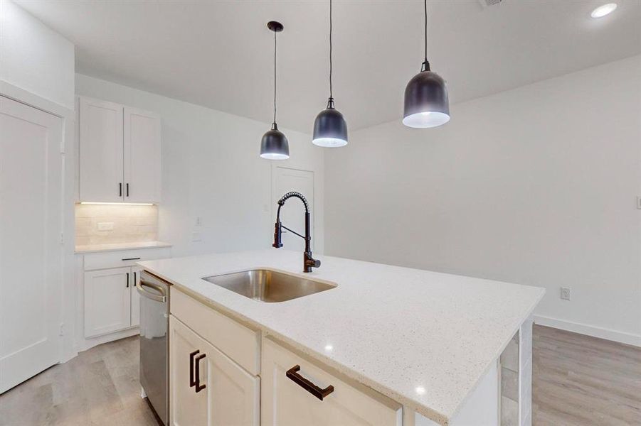 Kitchen featuring decorative light fixtures, backsplash, light wood-type flooring, an island with sink, and white cabinetry