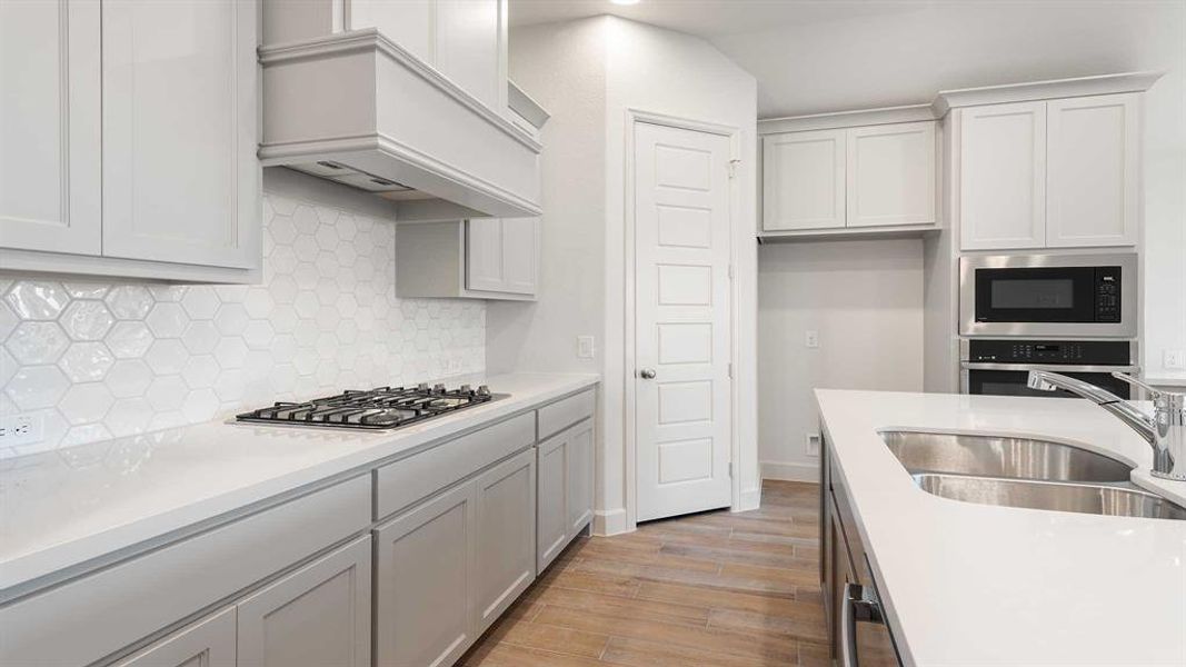 Kitchen with tasteful backsplash, light wood-type flooring, custom exhaust hood, appliances with stainless steel finishes, and sink