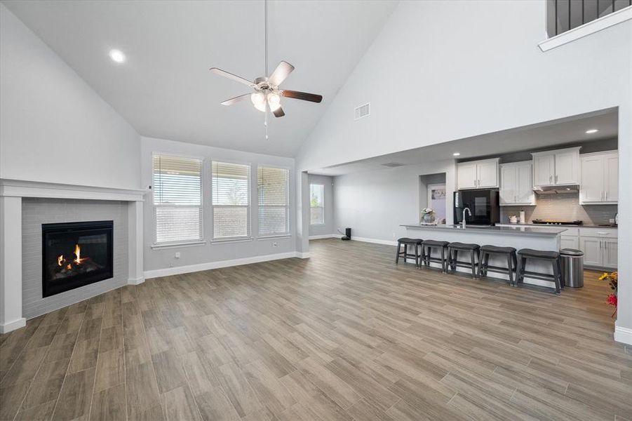 Living room featuring ceiling fan, light wood-type flooring, sink, and high vaulted ceiling