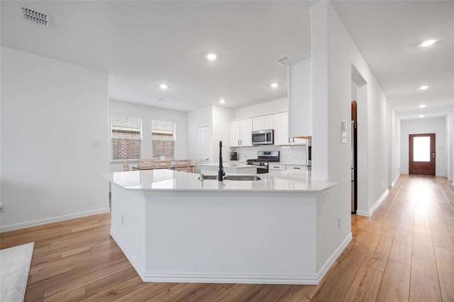 Kitchen with appliances with stainless steel finishes, sink, white cabinetry, light hardwood / wood-style flooring, and a center island with sink