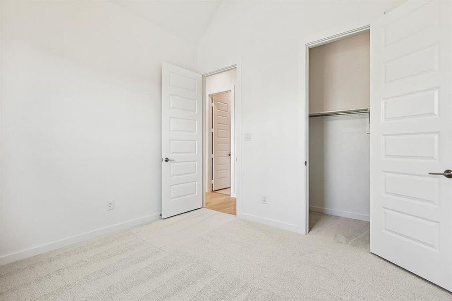 Unfurnished bedroom featuring vaulted ceiling, light carpet, and a closet
