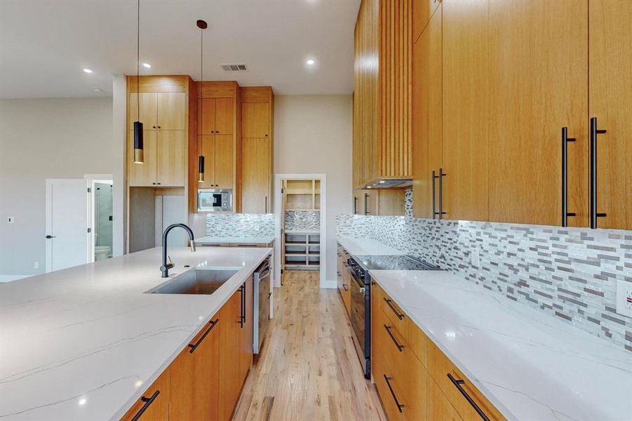 Kitchen featuring stainless steel appliances, sink, light wood-type flooring, light stone counters, and tasteful backsplash