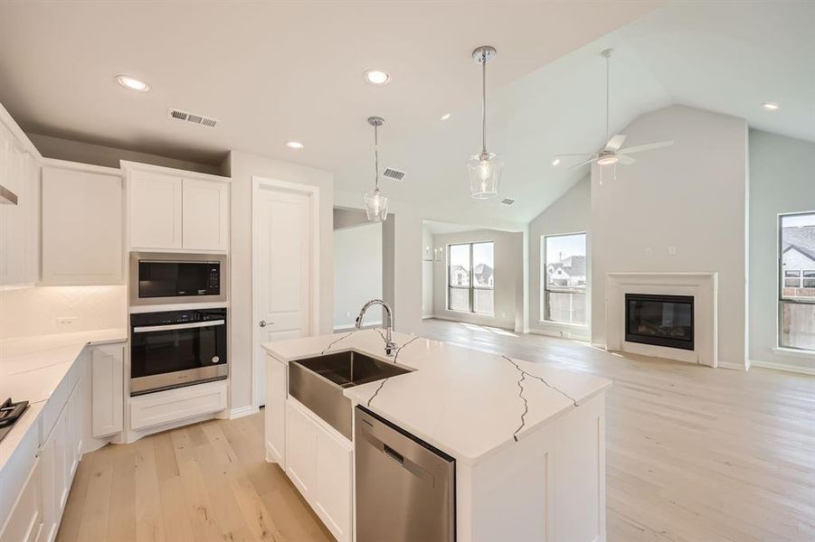 Kitchen featuring sink, stainless steel appliances, vaulted ceiling, white cabinets, and a center island with sink