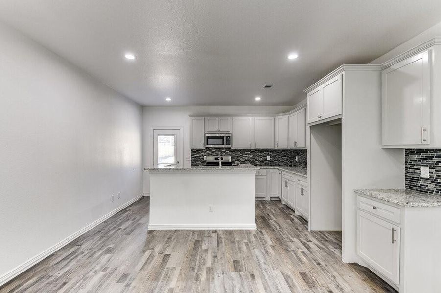 Kitchen with appliances with stainless steel finishes, white cabinets, light stone countertops, and light wood-type flooring