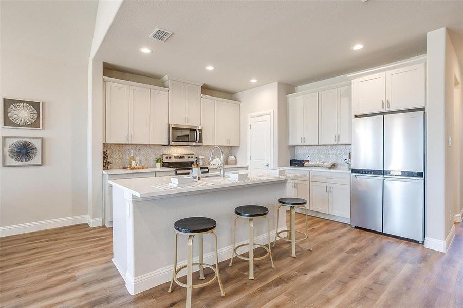 Kitchen featuring white cabinets, an island with sink, stainless steel appliances, and light wood-type flooring