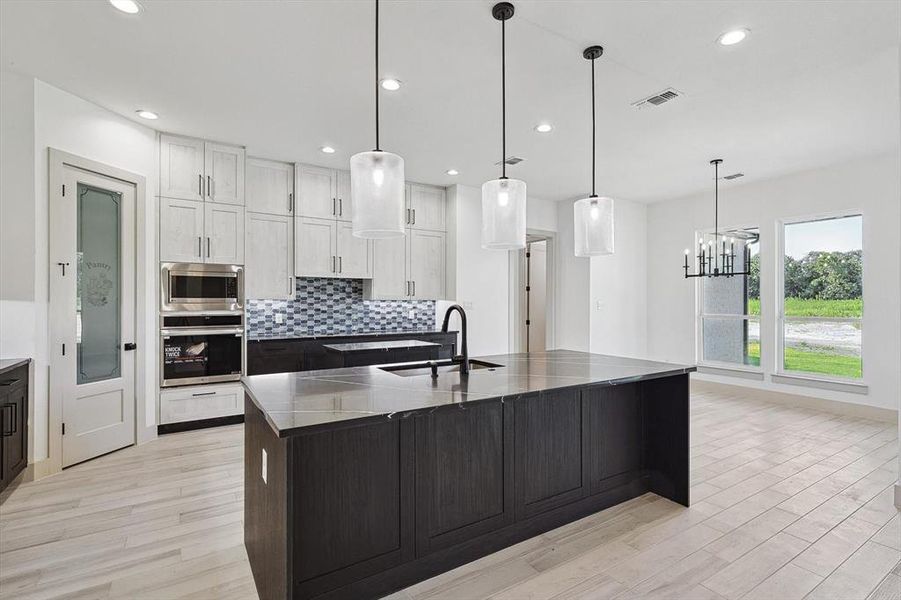 Kitchen with a kitchen island with sink, sink, appliances with stainless steel finishes, white cabinets, and light hardwood / wood-style floors