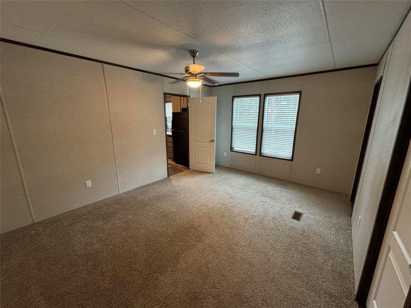 Unfurnished bedroom with light carpet, ceiling fan, black refrigerator, and a textured ceiling