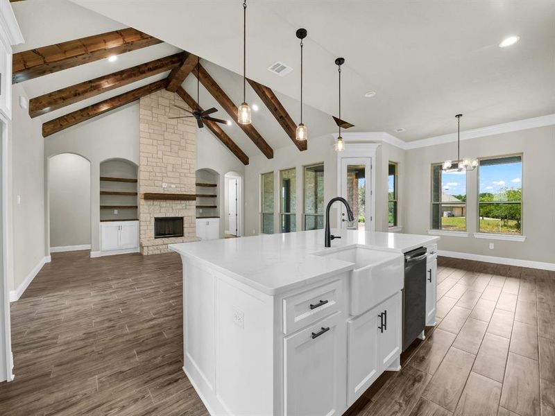 Kitchen with a kitchen island with sink, ceiling fan with notable chandelier, white cabinets, and a stone fireplace