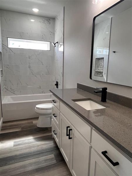 Full bathroom with wood-type flooring, vanity, tiled shower / bath combo, and toilet