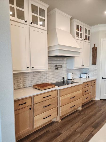 Kitchen with dark wood-type flooring, cooktop, decorative backsplash, extractor fan, and ornamental molding