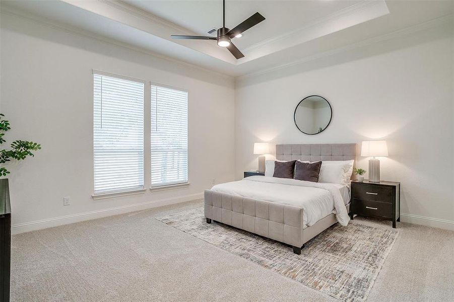 Bedroom with ornamental molding, light carpet, ceiling fan, and a raised ceiling