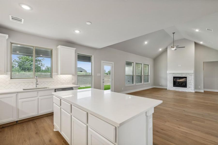 Kitchen with vaulted ceiling, white cabinetry, light wood-type flooring, a center island, and sink