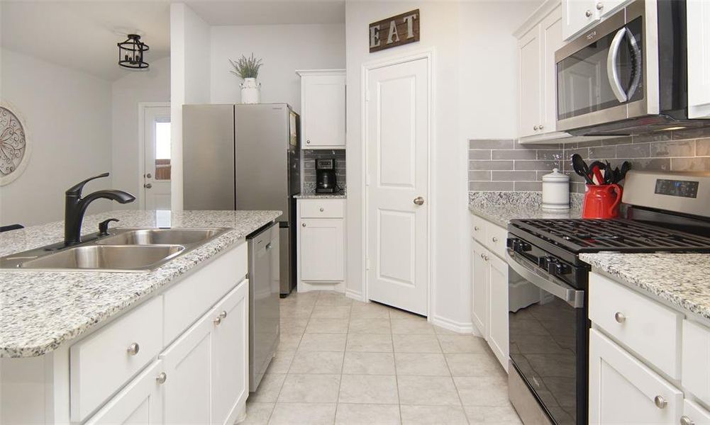 Kitchen with stainless steel appliances, decorative backsplash, sink, and white cabinets