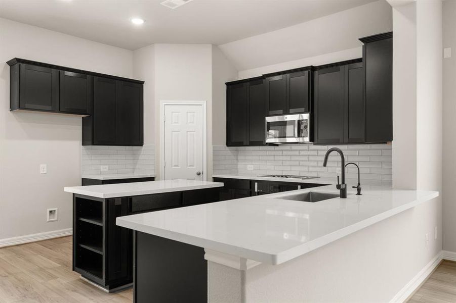 This light and bright kitchen features a large quartz island, dark stained cabinets, a large sink overlooking your family room, recessed lighting, and beautiful backsplash.