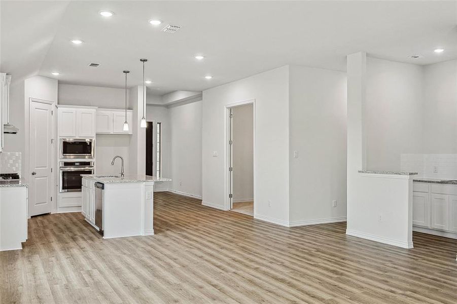 Kitchen with white cabinets, appliances with stainless steel finishes, an island with sink, and light hardwood / wood-style flooring