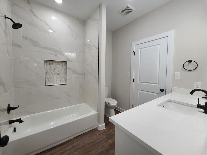 Full bathroom featuring hardwood / wood-style flooring, vanity, toilet, and tiled shower / bath combo