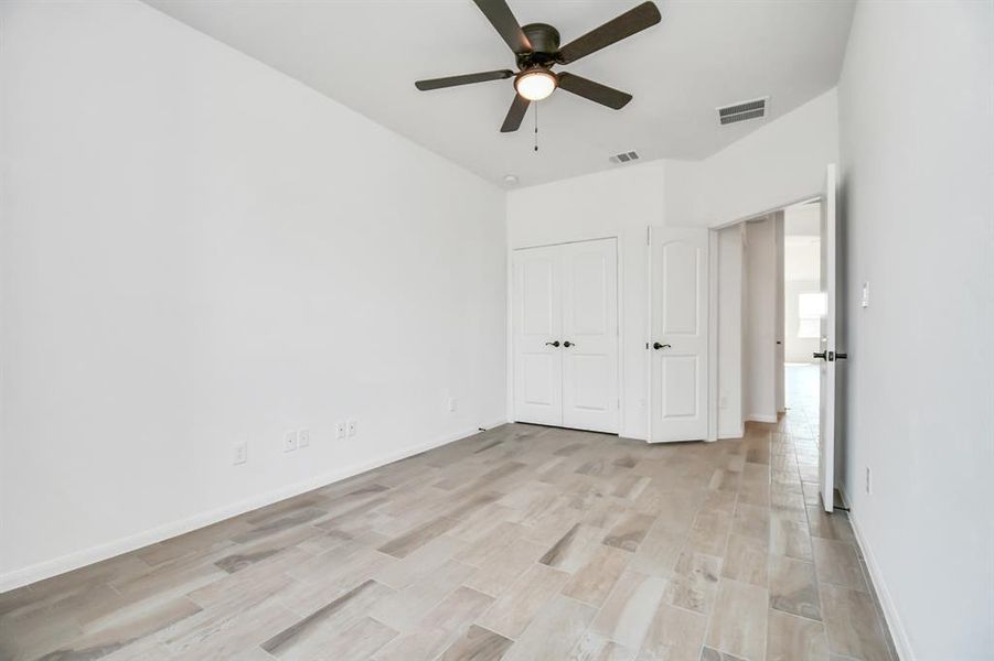 This is a bright, clean room featuring neutral walls, a ceiling fan with a light, and white double doors for closet storage.