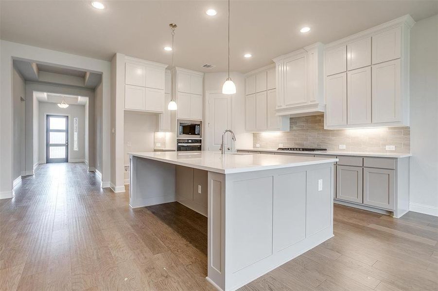 Kitchen with light hardwood / wood-style floors, sink, white cabinets, stainless steel appliances, and a center island with sink