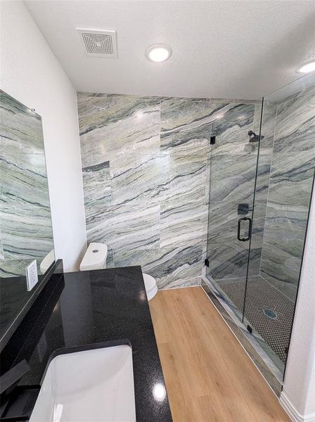 Bathroom featuring sink, a textured ceiling, hardwood / wood-style flooring, toilet, and a shower with door