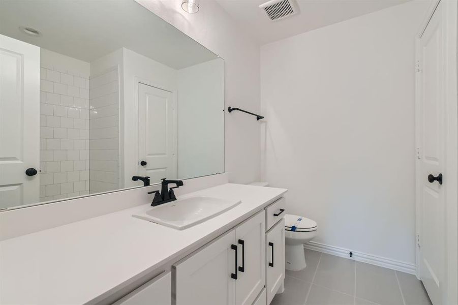 Bathroom featuring vanity, toilet, a tile shower, and tile patterned flooring