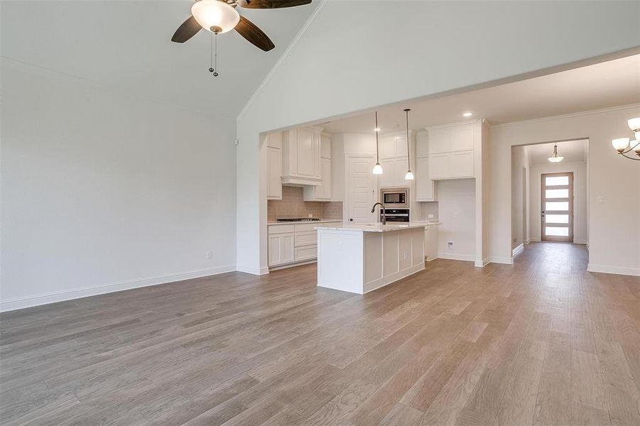 Kitchen featuring an island with sink, appliances with stainless steel finishes, light wood-type flooring, and high vaulted ceiling