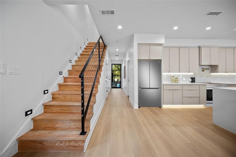 Kitchen with white cabinets, oven, light wood-type flooring, and stainless steel fridge