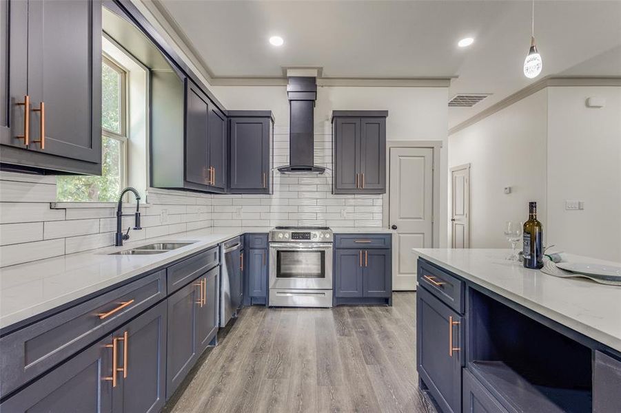 Kitchen featuring light hardwood / wood-style flooring, appliances with stainless steel finishes, wall chimney exhaust hood, sink, and ornamental molding